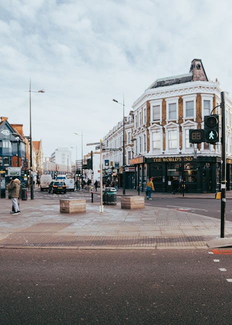 A busy London street scene in NW1 Camden featuring classic white Victorian-style buildings with large windows and decorative stonework. Several red double-decker buses are parked along the street, and